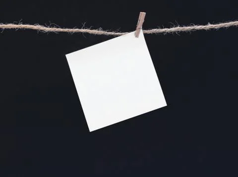 A white square piece of note paper hangs on clothespins on a black background Stock Photos