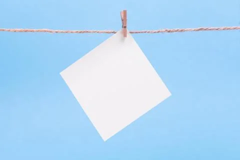 A white square piece of note paper hangs on clothespins on a blue background, Stock Photos