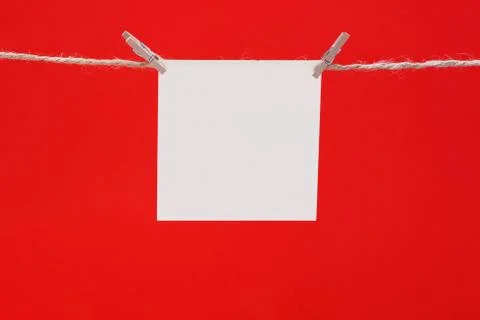 A white square piece of note paper hangs on clothespins on a red background,  Stock Photos