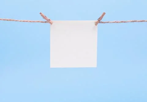 A white square piece of note paper hangs on clothespins on a blue background, Stock Photos