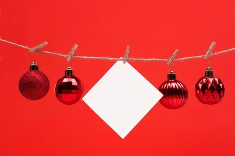 A white square piece of note paper hangs on clothespins on a red background w Stock Photos