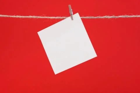A white square piece of note paper hangs on clothespins on a red background Stock Photos