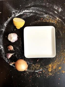 A white square plate on a black table decorated with spices. Foto stock