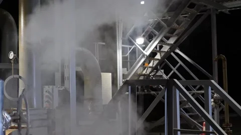 White steam billows from a pipe in an industrial setting, illuminated by nearby Stock Footage 295489823