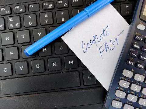A White sticky note with text COMPLETE FAST and pen,calculator on top of lapt Stock Photos