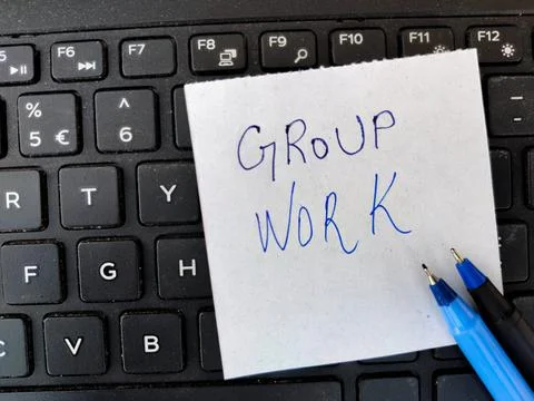 A White sticky note with text GROUP WORK and two pens on top of laptop keyboa Stock Photos