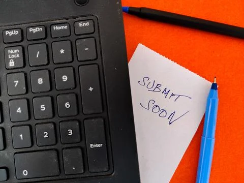 A White sticky note with text SUBMIT SOON kept under Laptop. Orange backgroun Stock Photos