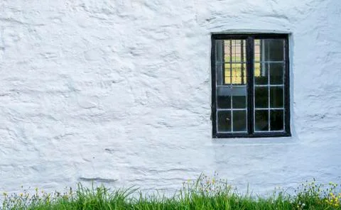 White, stone wall with a black window frame and grass Stock Photos