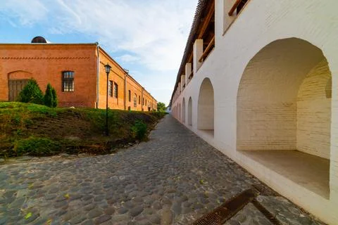White stone wall of the courtyard with large arches and a wooden roof along t Stock Photos