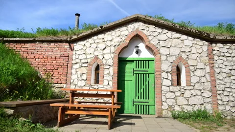 A white stone wine cellar with a green door and an orange picnic table in front, Stockbeeldmateriaal 342228839
