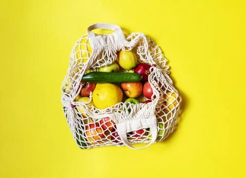 White string bag with different vegetables and fruits on a yellow background Stock Photos