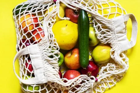White string bag with different vegetables and fruits on a yellow background Stock Photos