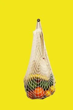 White string bag with different vegetables and fruits on a yellow background. Stock Photos