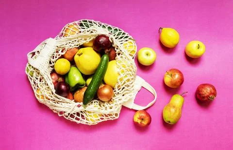 White string bag with different vegetables and fruits on a pink background. top Stock Photos