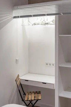 White study table combined with wardrobe with wooden shelves and a chair in a Stock Photos