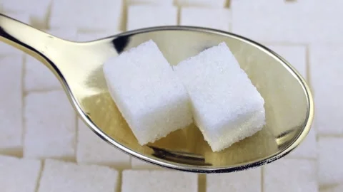 White sugar cubes in the spoon on sugar grains background circle rotation Stock Footage 243560416
