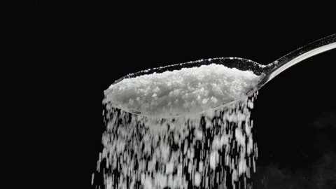 White sugar falling in slow motion on spoon on black background. Pouring sugar. Stockbeeldmateriaal 329435402