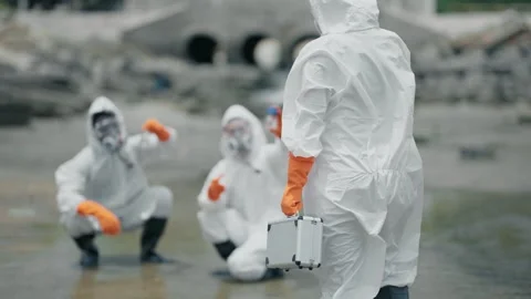 White suits cover workers in muddy, industrial zone 스톡 동영상 346120313