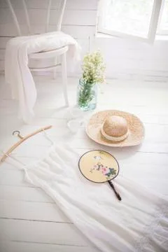 White summer dress and straw hat and handheld fan on the floor. Stock Photos