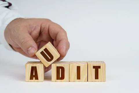 On a white surface, a man stacks cubes with the inscription - AUDIT Foto stock