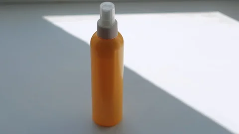 On a white surface an orange colored bottle is picked up by a man's hand Stock Footage 128324154
