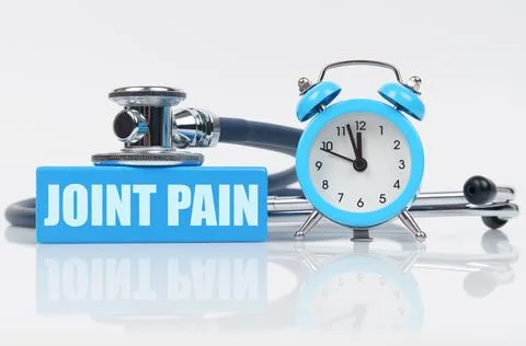 On a white surface there is an alarm clock, a stethoscope and a blue block wi Stock Photos