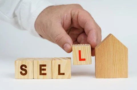 On a white surface there is a model of a house, next to it a man has placed.. Stock Photos