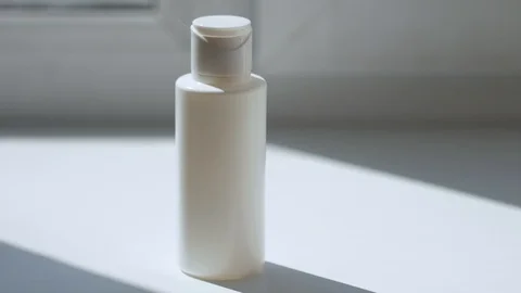 On the white surface is a white bottle, a hand in the frame picks it up close-up Stock Footage 128323945
