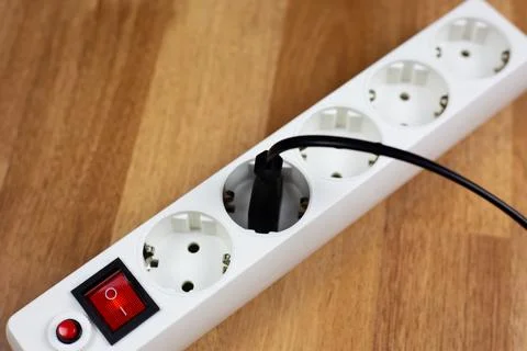 White surge protector with red switch and safety button rests on wood. Dark.. Stock Photos