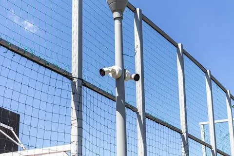 White Surveillance Security Camera Mounted on Sports Field Fence Post Stock-Fotos