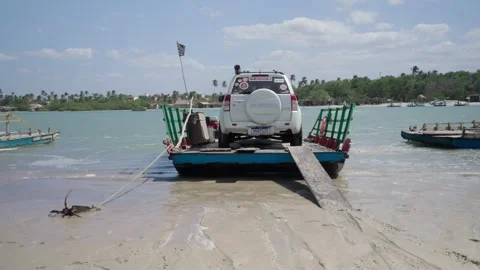 A white SUV being transported across a tropical river on a traditional wooden Видео 335266879