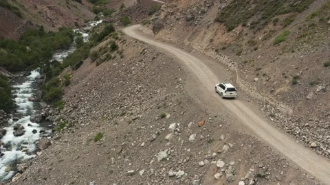 White SUV Driving Along River in Rocky Valley, North Pakistan, Aerial Follow Stock Footage 131821811