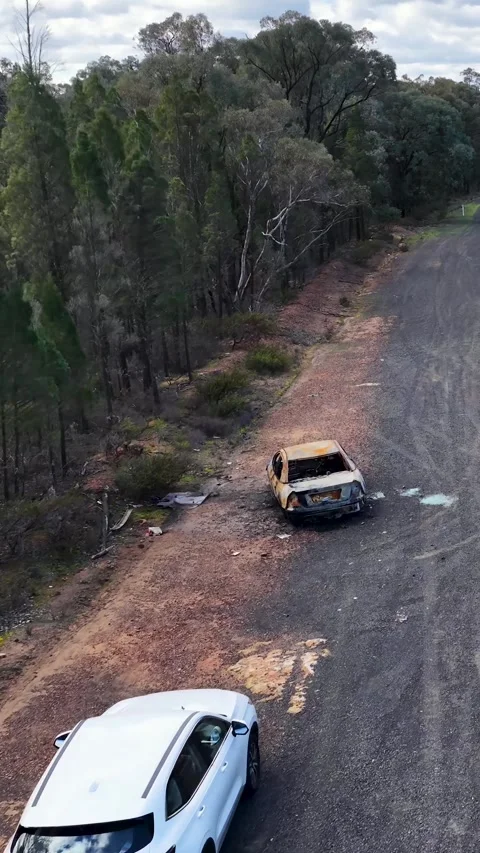 White SUV Driving Past Burnt Car Wreck on Outback Road Stock Footage 340863451