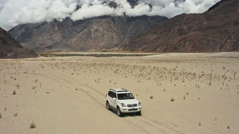 A white SUV driving slowly through a Cold Desert surrounded by mountains Stock Footage 132295566