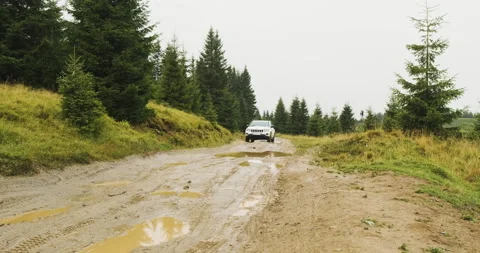 White SUV overcomes mud and puddles on the roads among the forest with fir trees 動画素材 192005170