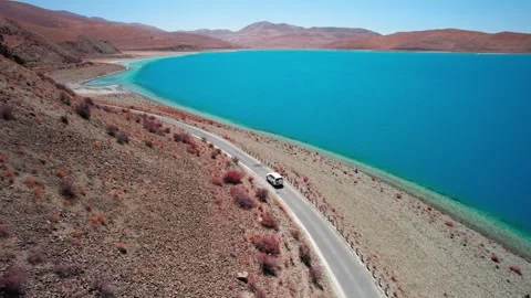 White SUV rounding a lakeside curve in the Tibetan plateau 스톡 동영상 345884907