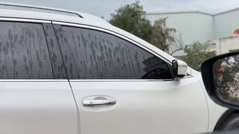 White SUV Side Window with Rain Drops Parked Outdoors Near Buildings 스톡 동영상 332791490