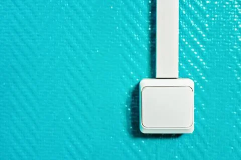 White switch with a cable channel on a turquoise wall. Stock Photos