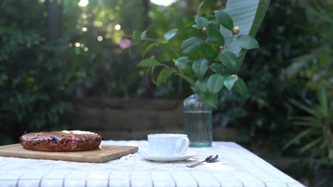 White table with a berry pie, cup, sucer and a tea spoon, vase and flowers. Stock Footage 141014745
