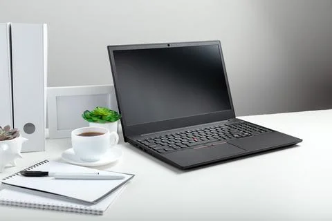 White table with laptop for remote work or study. Black laptop with blank dis Stock Photos
