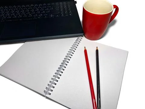 On a white table lies a notebook with colored pencils, red and black. Stock Photos