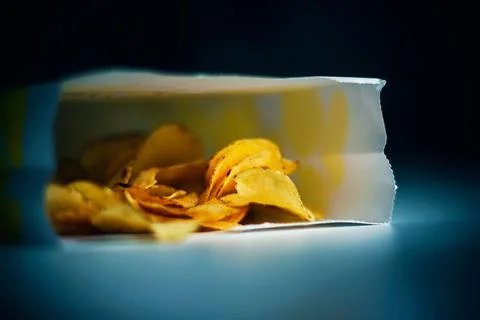On the white table is a paper bag of chips, lit by the bluish light from the  Stock Photos