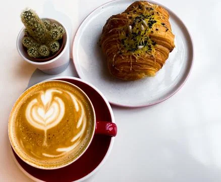 On a white table is a red cup of coffee, a bun with cheese and black sesame s Stock Photos