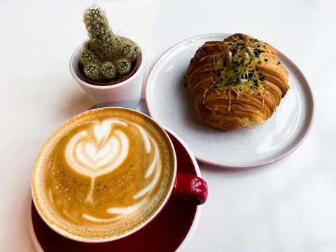 On a white table is a red cup of coffee, a bun with cheese and black sesame s Stock Photos