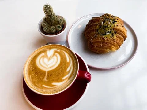 On a white table is a red cup of coffee, a bun with cheese. Stock Photos