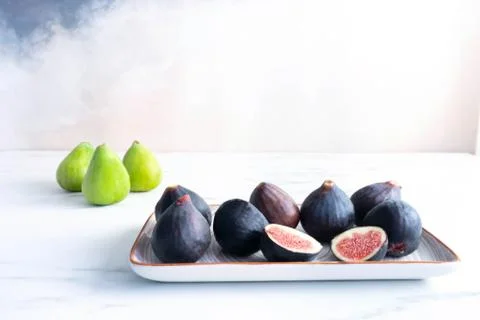 On a white table stands a rectangular platter full of ripe purple figs Photos