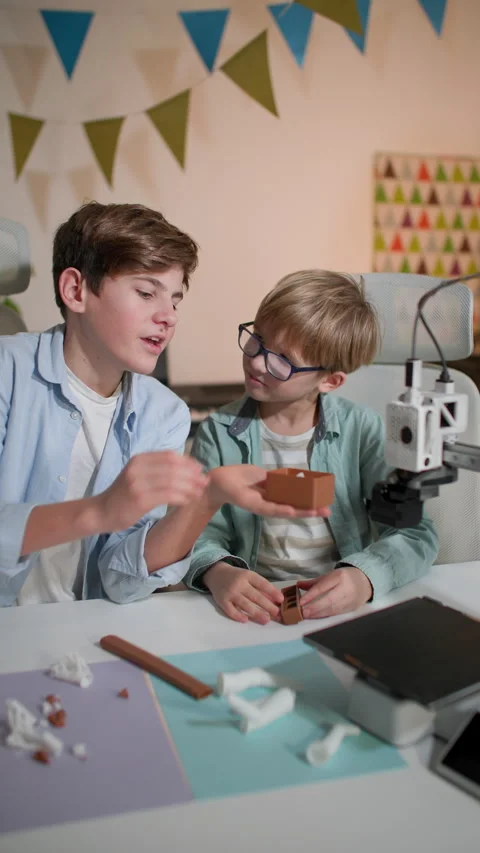 At a white table, two kids stop a 3D printer and take away the printed part Stock Footage 335392404