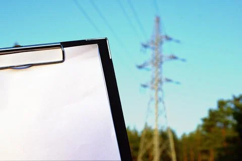 White tablet on the background of a power grid tower. Energy concept. Copy sp Stock Photos