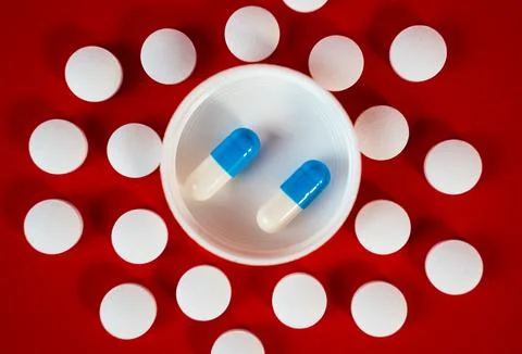 White tablet grid with central lid holding two blue capsules on red Stock Photos