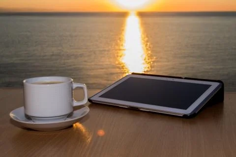 White tablet ipad on table desk with coffee cup during sunset, with sun Stock Photos